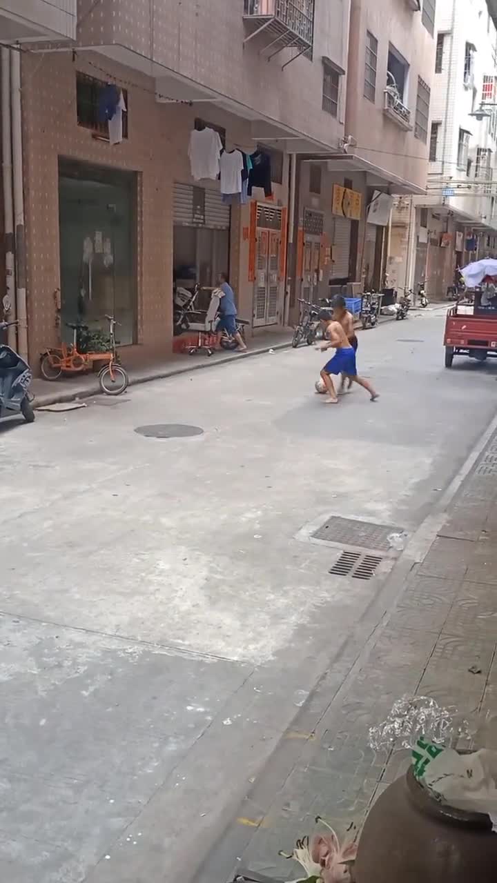 这球比手机好玩吗？俩小孩衣服都不穿在街头踢球